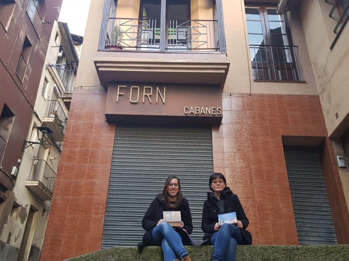 La regidora Roser Valverde i la tècnica Marta Planas davant de l'antic Forn Cabanes, una de les imatges del calendari.