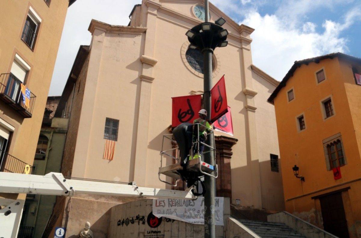 Uns operaris instal·len cartells a la plaça de Sant Pere. 