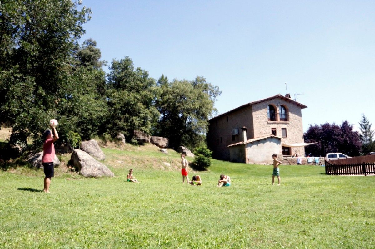 Un dels hostes de la Barraca de Casseres, amb els nens, jugant a futbol amb la masia al fons.