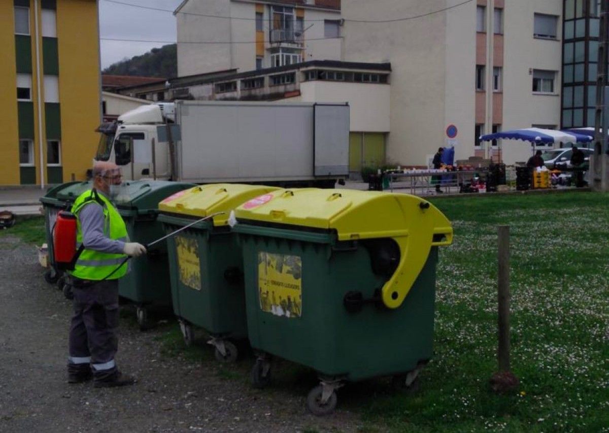 Un treballador de la brigada municipal desinfecta uns contenidors de brossa.