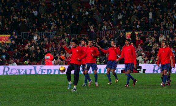 Els jugadors del Barça sobre la gespa de Royalverd i amb l'anunci de l'empresa de fons al Camp Nou.