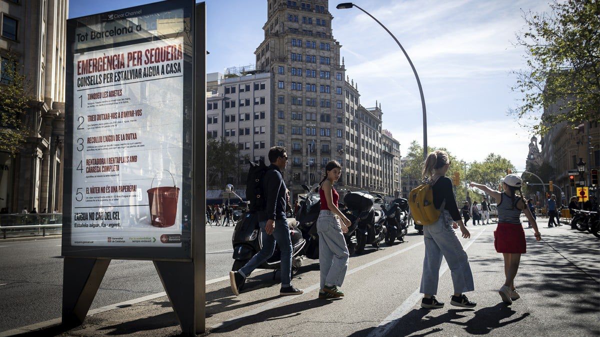 Una família de turistes passeja a Barcelona a tocar d'un anunci sobre la sequera