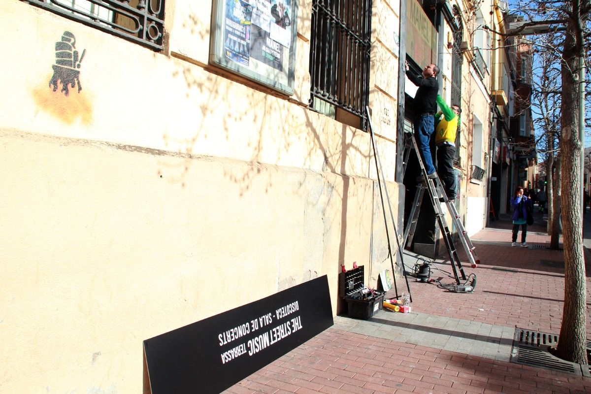 Uns operaris col·loquen el cartell de The Street Music a la porta del local, aquest divendres.