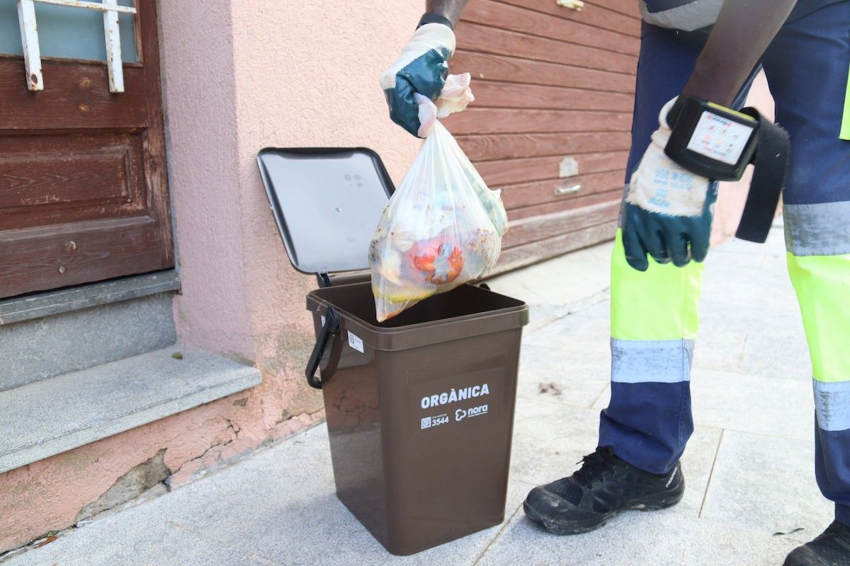 Un operari traient una bossa d'escombraries del cubell de la fracció orgànica.