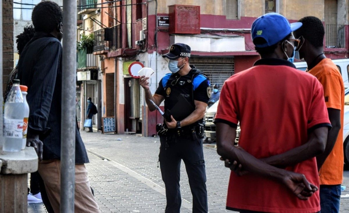 Un policia ensenyant una mascareta a un grup d'immigrants 