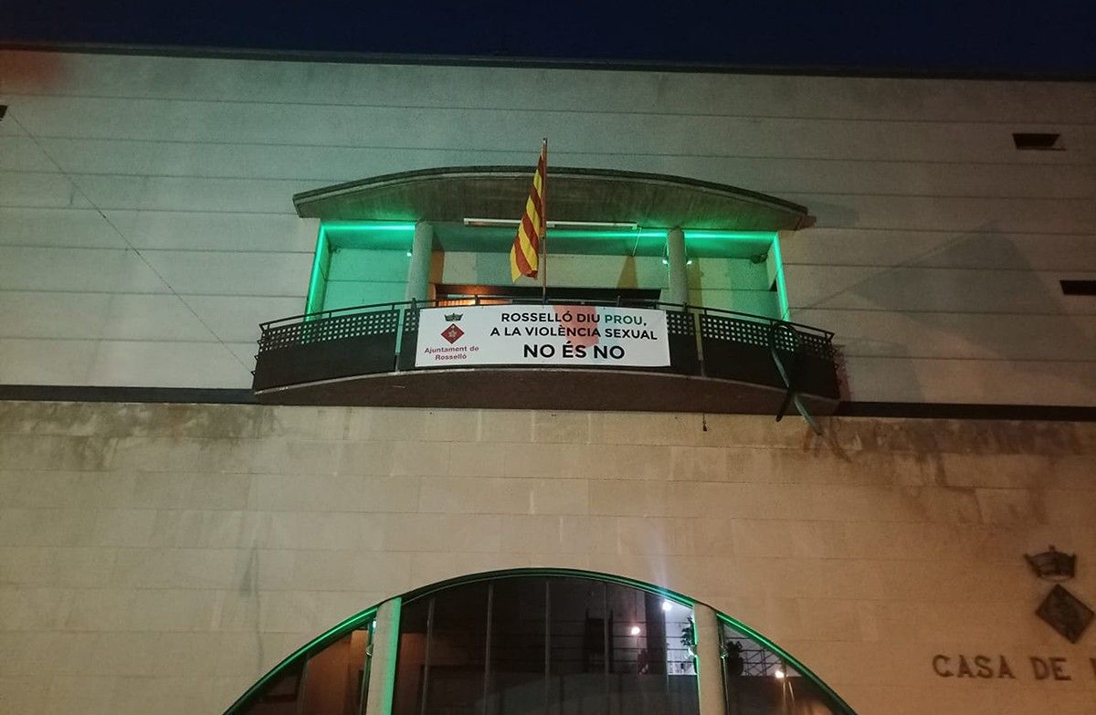 La façana de l'Ajuntament de Rosselló il·luminada de verd i amb una pancarta en senyal de rebuig de les agressions sexuals.
