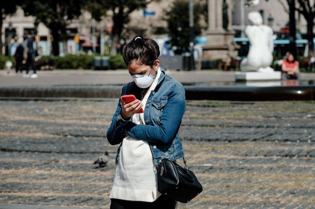 Una noia amb mascareta mira el telèfon mòbil