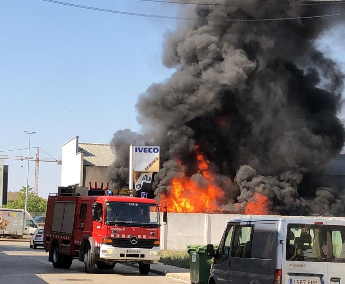 Flames de l'incendi en un solar al costat d'un taller a Tàrrega i un camió de Bombers al davant.
