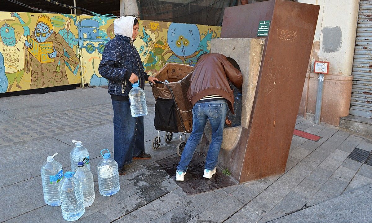Gina i Nikolai omplint garrafes a la font pública de la plaça del Carme