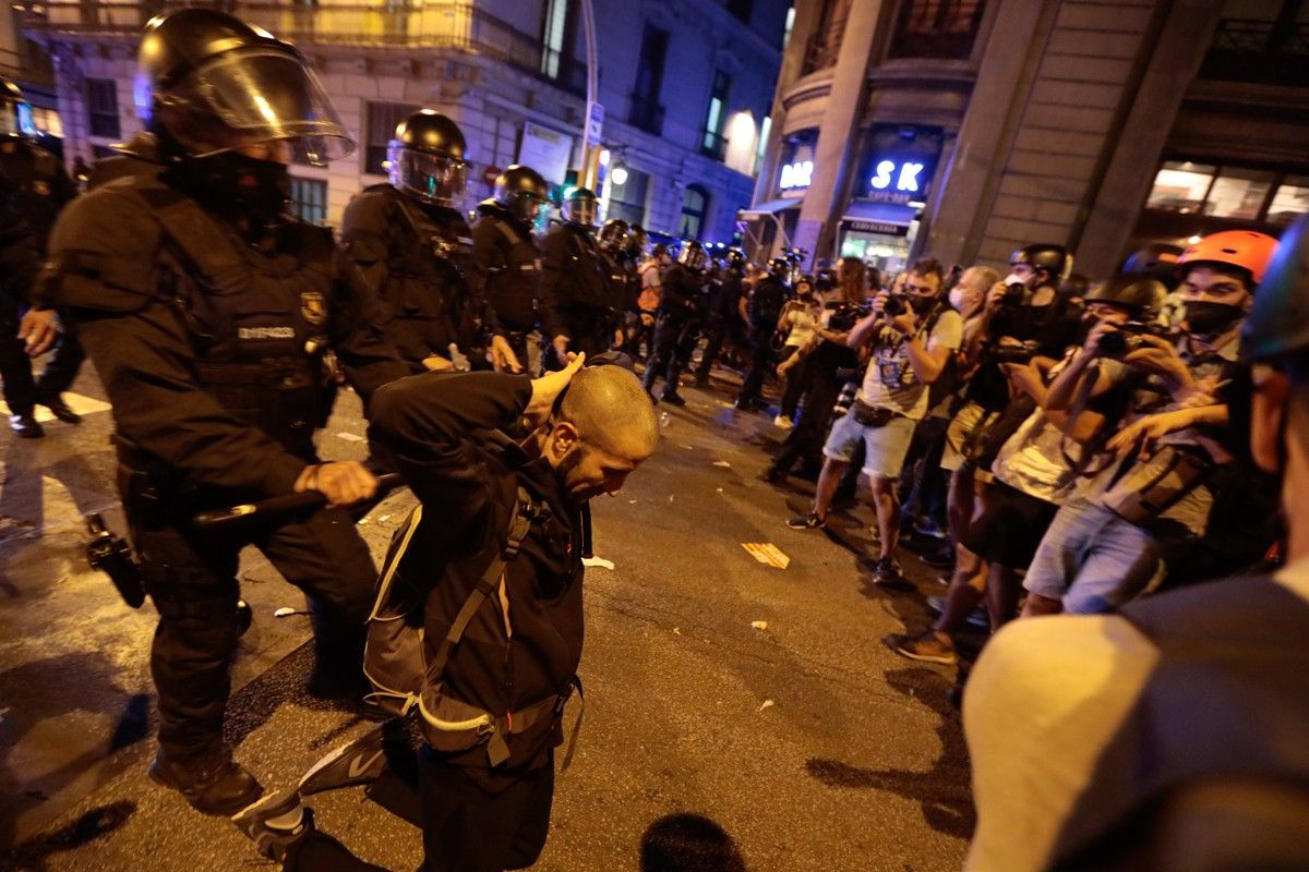 Un home s'agenolla amb les mans al clatell d'esquena a un agent dels Mossos d'Esquadra a la Via Laietana de Barcelona