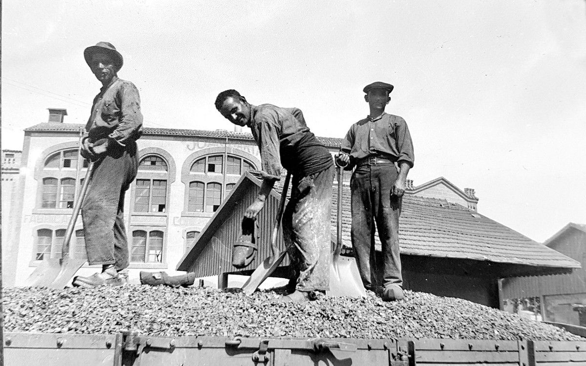 Treballadors, calçats amb esclops, en la descàrrega de vagons, a l'actual plaça del Mil·lenari de Catalunya. Al fons, la farinera Albareda