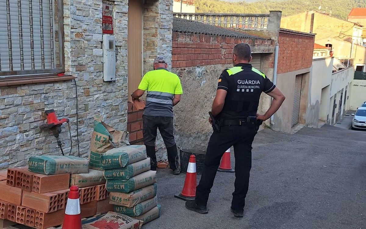 Un operari tapia la porta de la casa custodiat per un agent de la Guàrdia Municipal de Castellbell