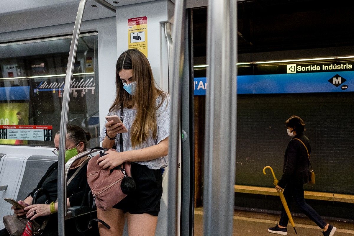 Una noia mirant el telèfon mòbil a l'L5 del Metro de Barcelona, estació Camp de l'Arpa
