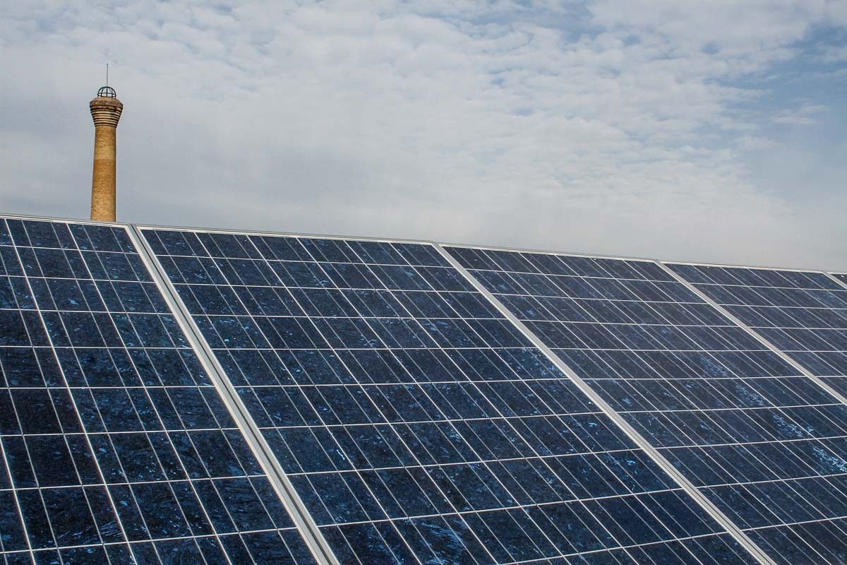 Uns panells fotovoltaics amb una xemeneia al fons, a la comarca d'Osona. 