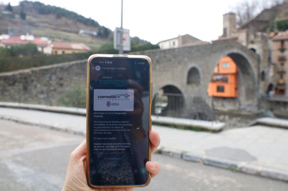 Un mòbil amb la guia turística i el pont romànic de fons