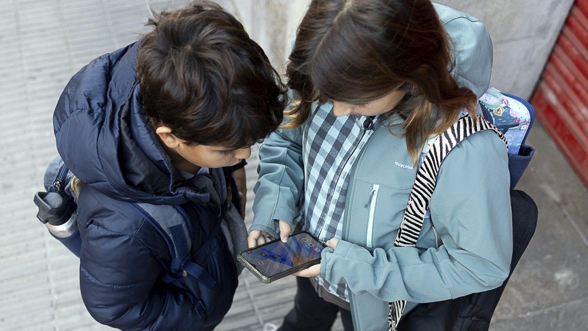Dos alumnes utilitzen els seus mòbils a l'entrada de l'escola