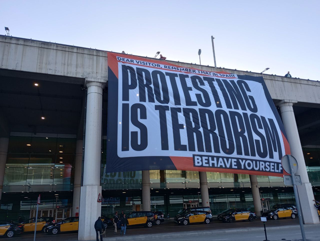La pancarta que Òmnium ha penjat a l'aeroport del Prat per denunciar la causa de Tsunami Democràtic