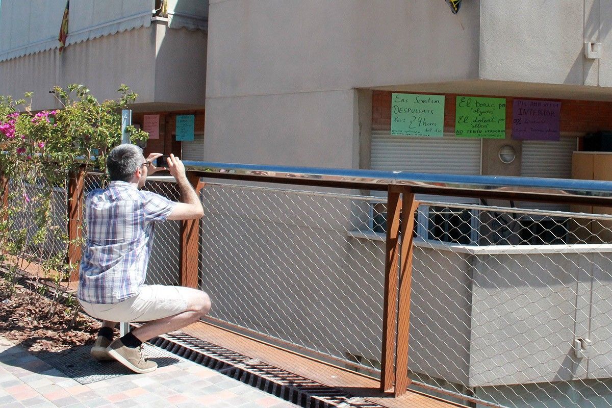 Un home fotografia els cartells de protesta que penjats a un balcó afectat