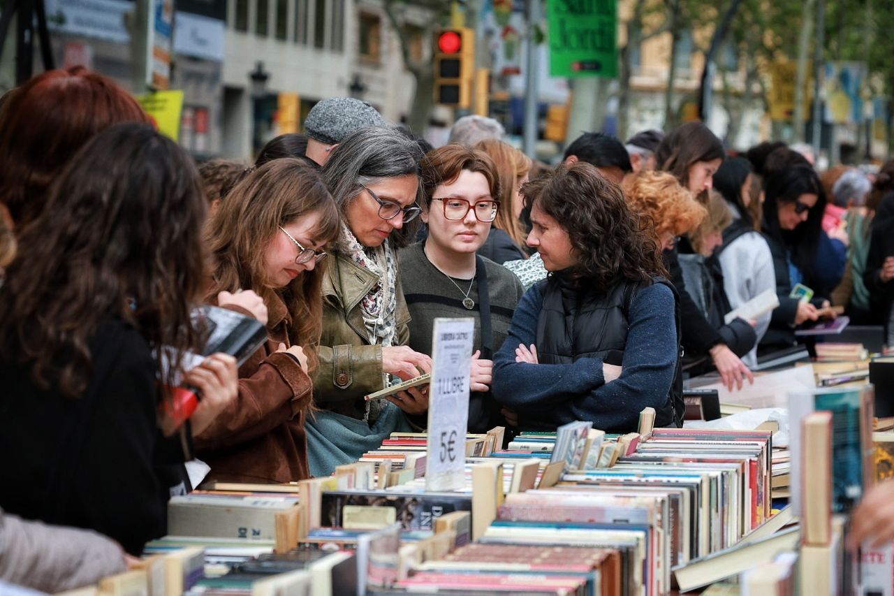 Un grup de persones remena llibres en una parada per Sant Jordi
