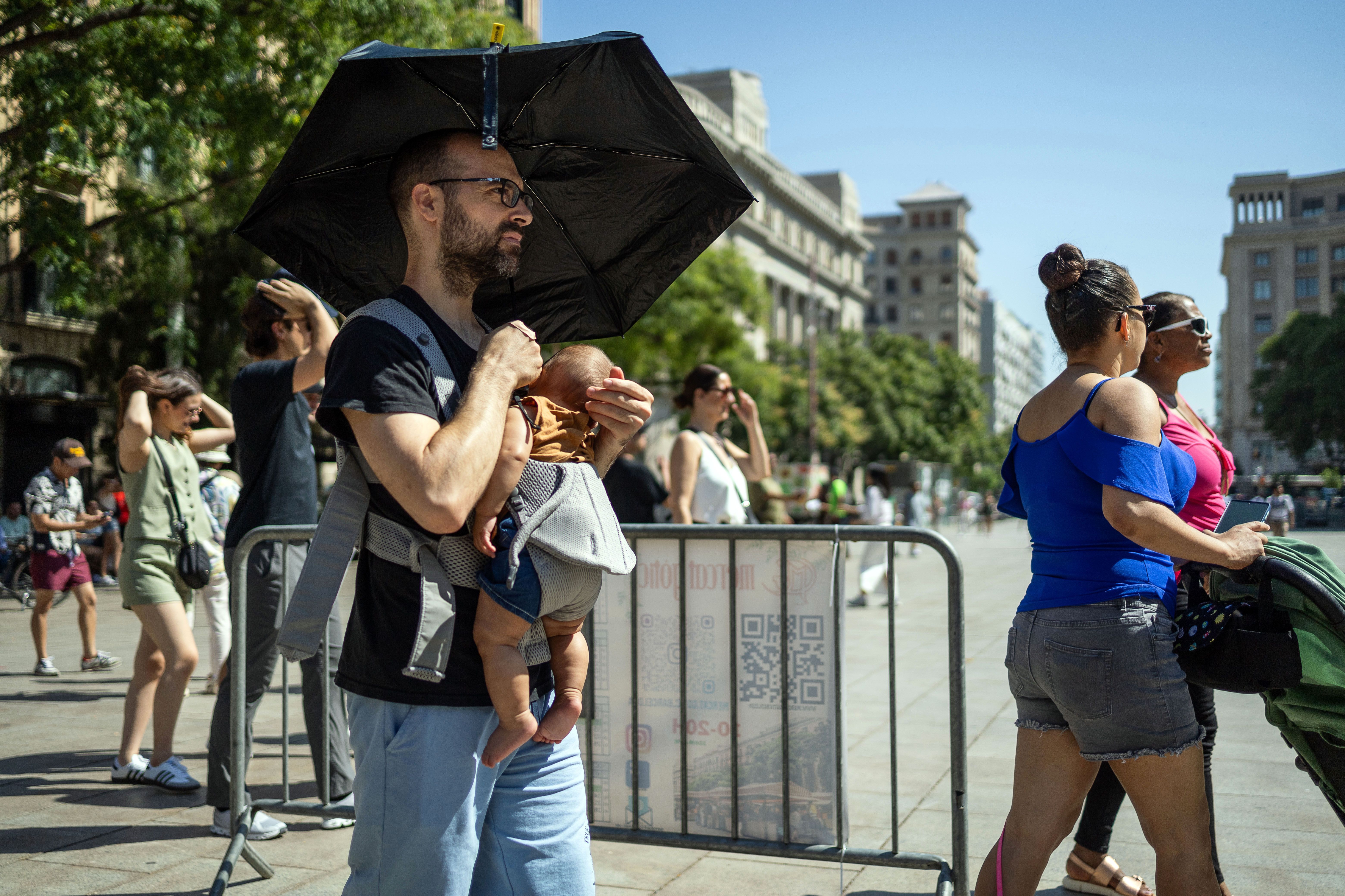 Un turista es protegeix a ell i al seu nadó del sol al centre de Barcelona