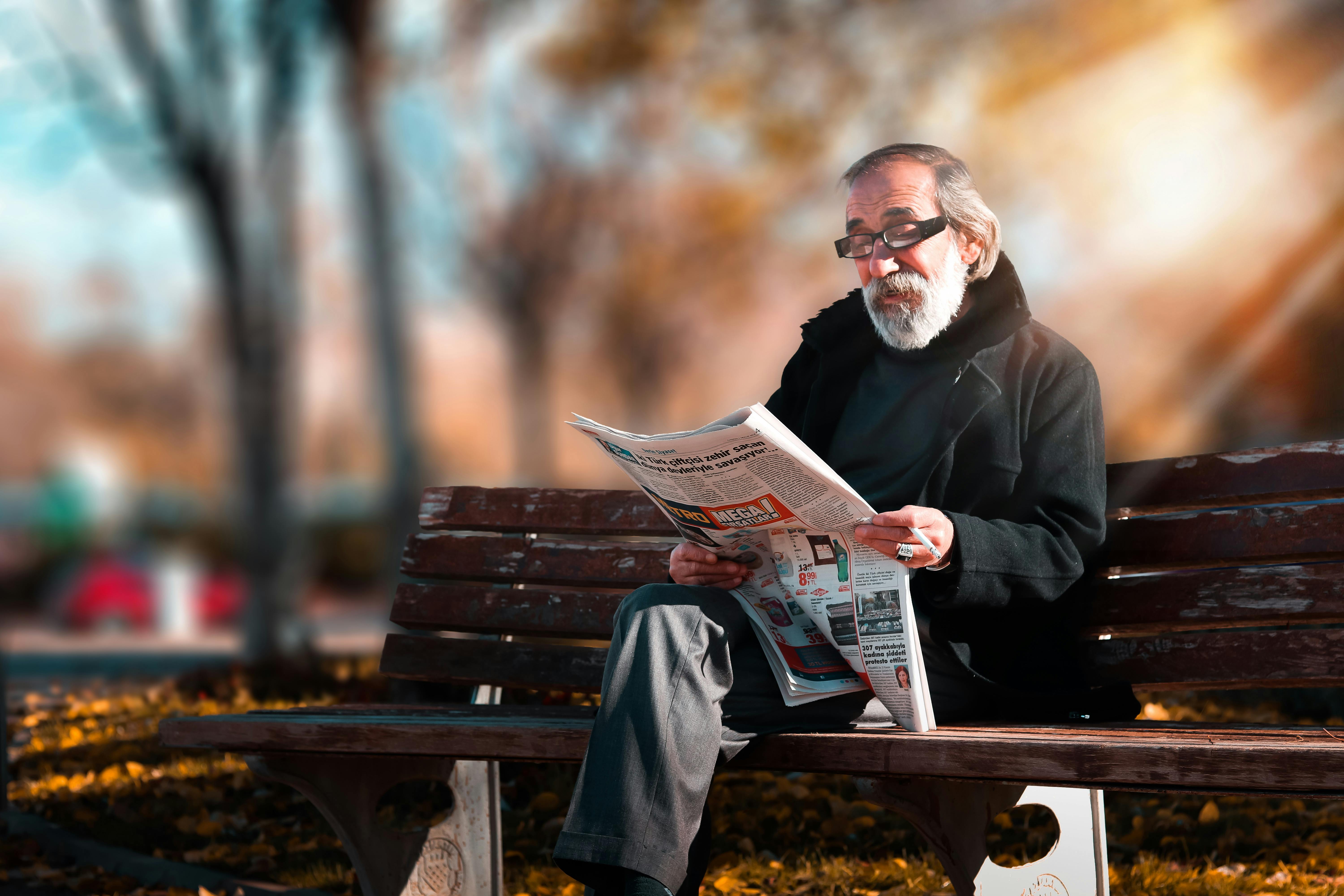 Un home assegut en un banc llegint el diari