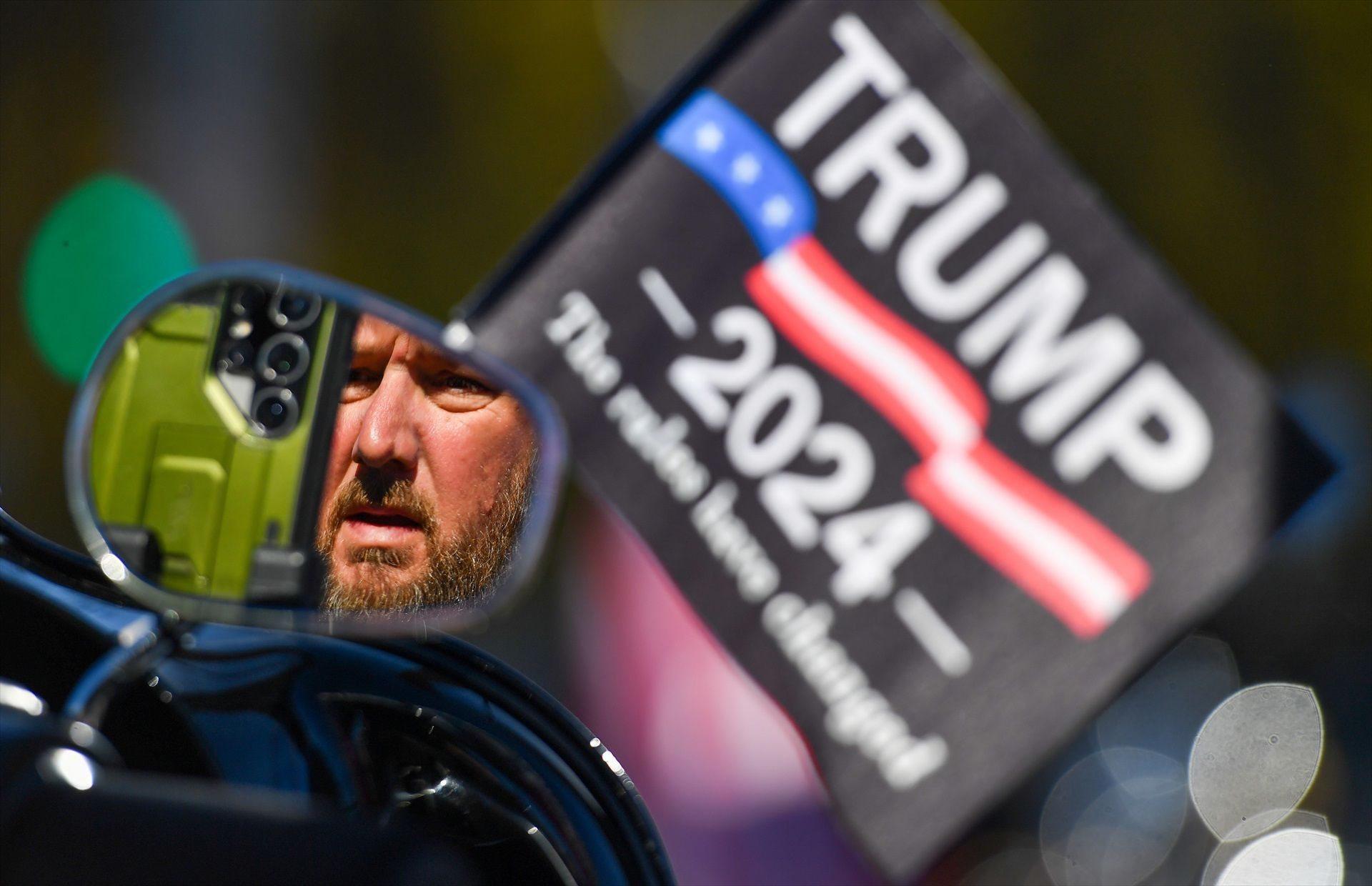 Un motorista es mira al mirall darrere una bandera de Trump