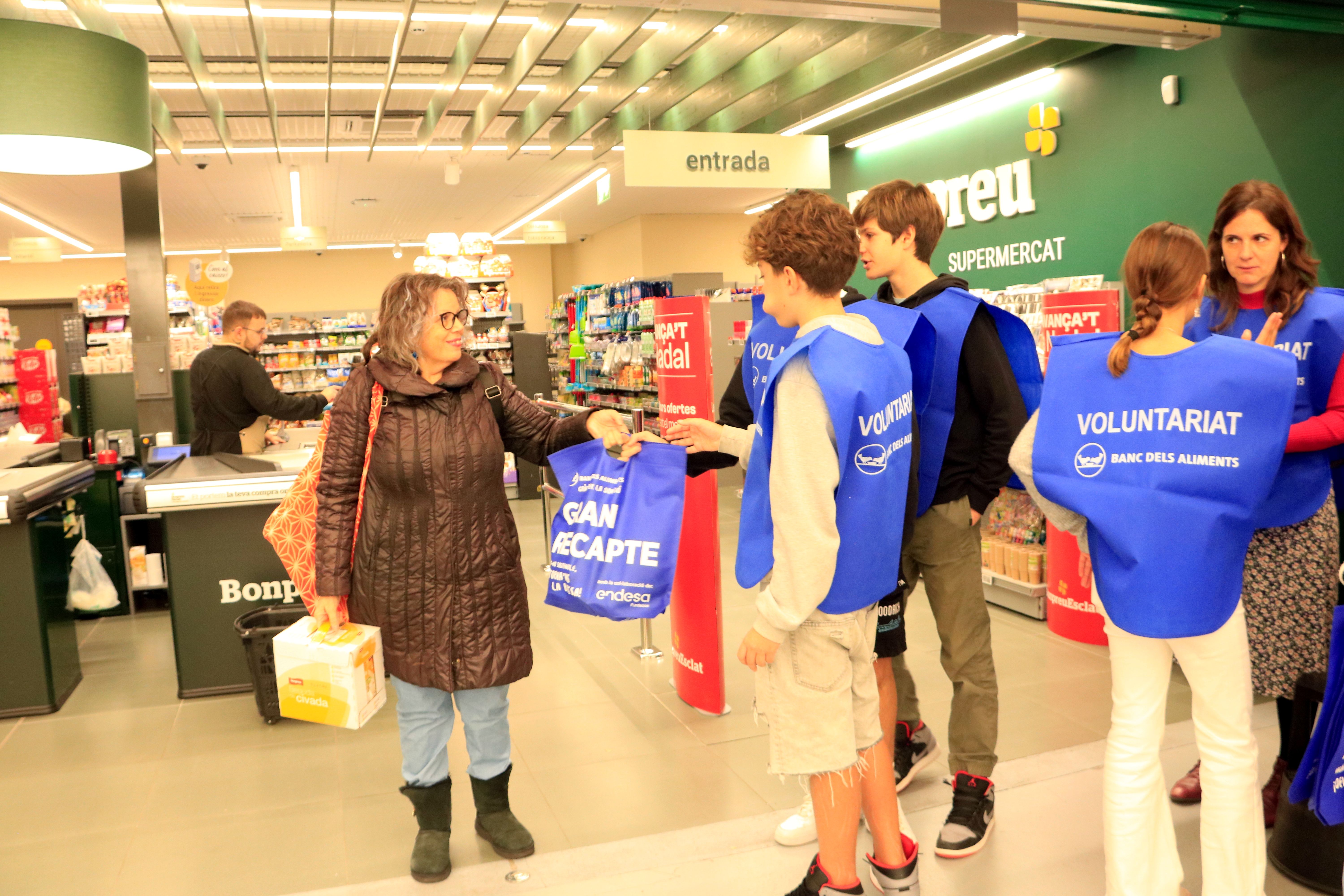 Voluntaris del Gran Recapte entreguen una bossa a una dona a l'entrada d'un supermercat