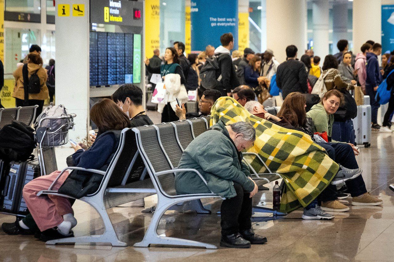 Una persona sense llar dorm, coberta per una manta, a l'aeroport de Barcelona