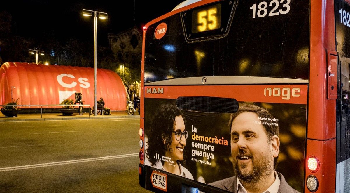 Un cartell electoral d'ERC en un autobús urbà, davant de la carpa de Ciutadans al centre de Barcelona