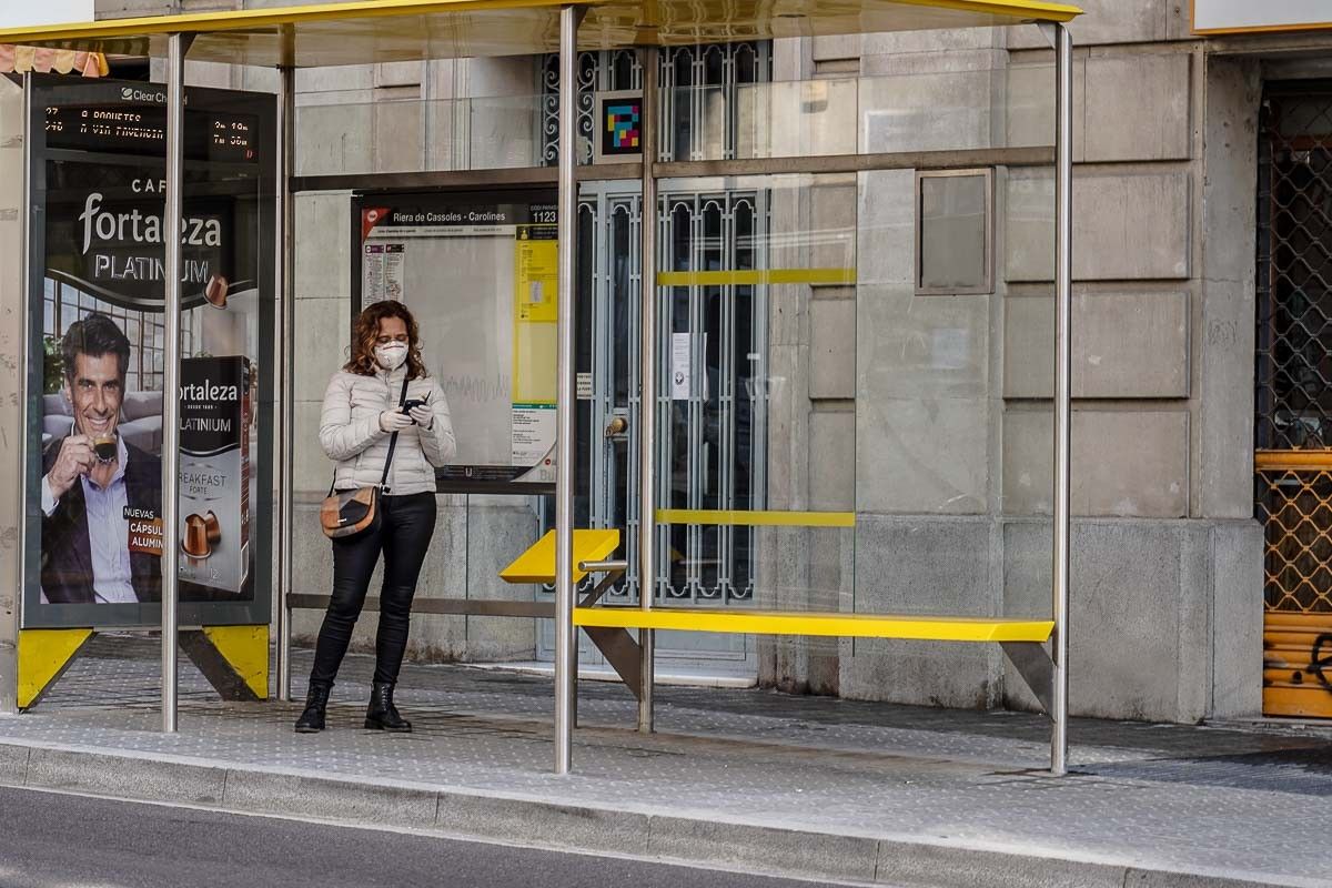 Una dona amb mascareta espera l'autobús en una parada de Barcelona. 