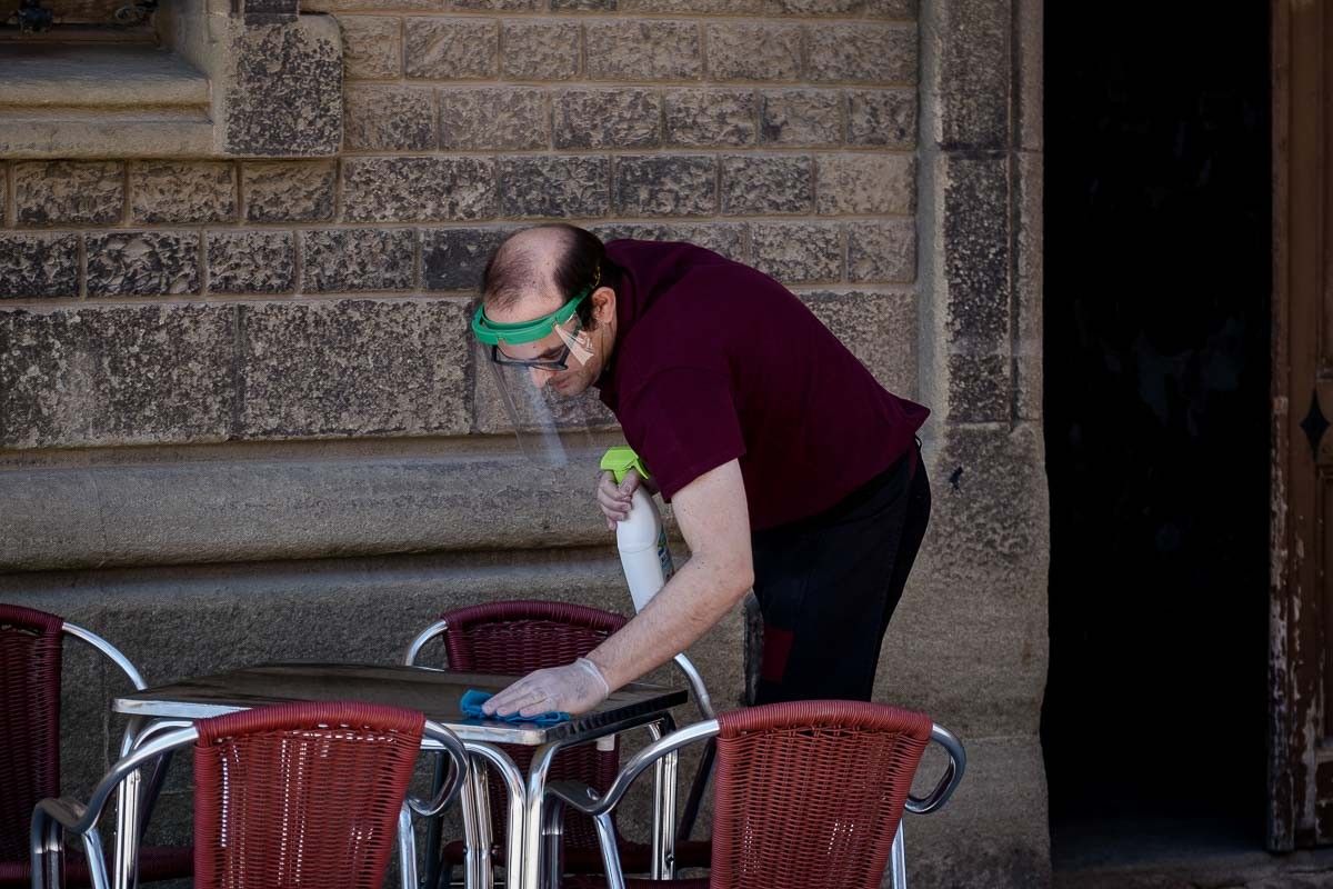 Un cambrer, amb una pantalla facial, desinfecta una taula de la terrassa.
