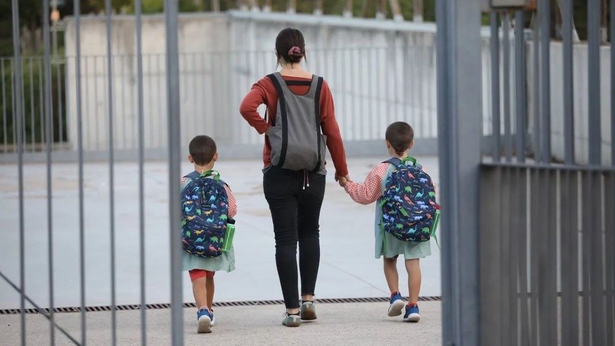 Dos nens acompanyats de la seva mare entrant a una escola