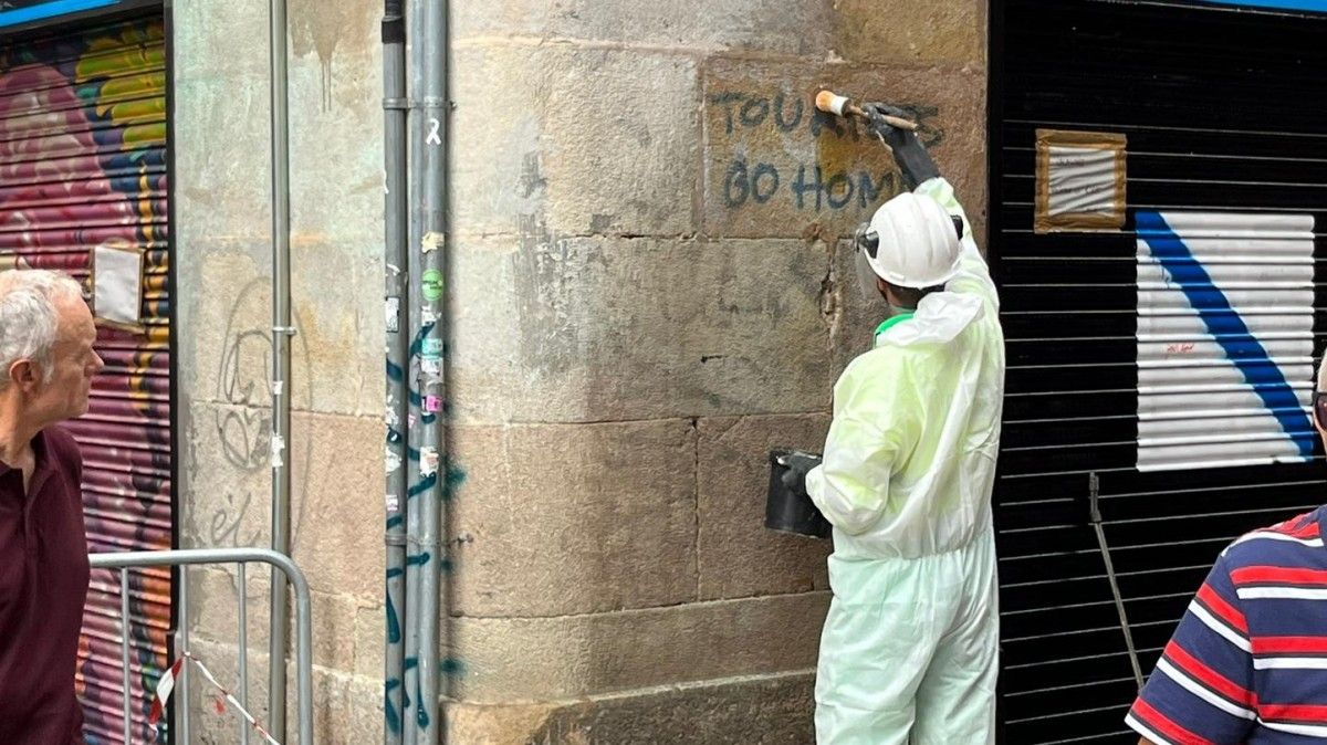 Un operari de neteja de l'Ajuntament de Barcelona esborra una pintada de 