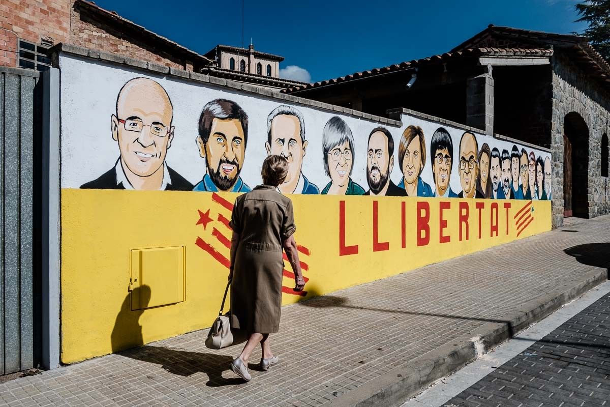 Una dona passa davant dels retrats de Raül Romeva i la resta d'exiliats i presos polítics, pintats en un mur de Folgueroles