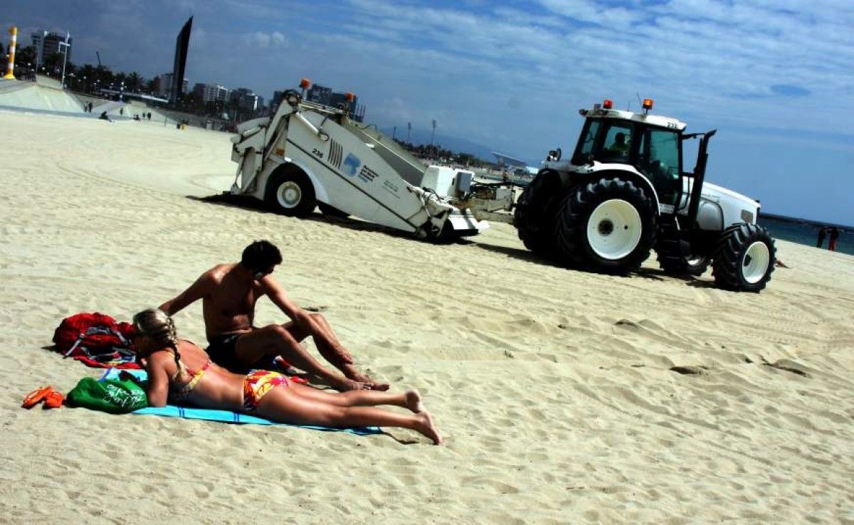 Una parella en una platja, mentre un tractor la neteja