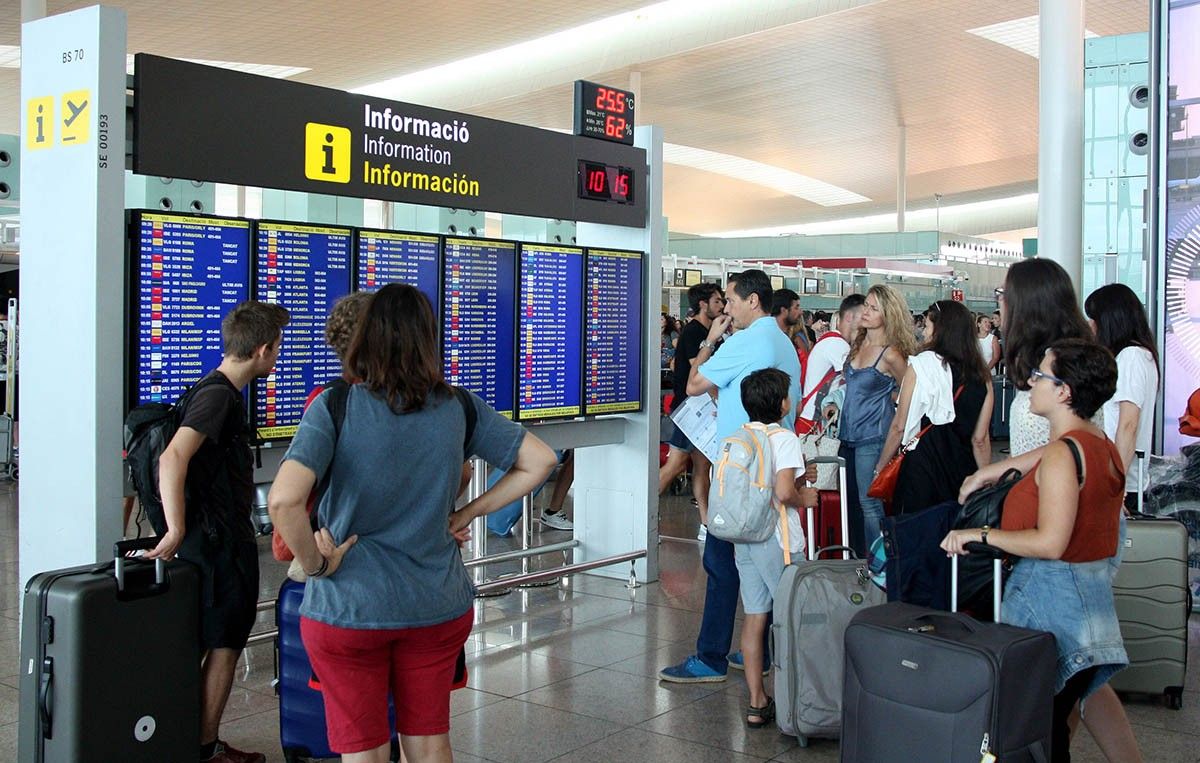 Diversos passatgers consulten el llistat de sortides de la T1 de l'aeroport del Prat