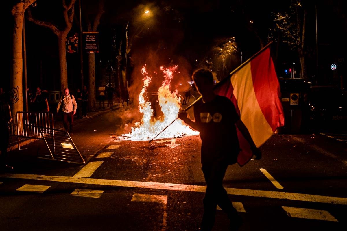 Un jove amb una bandera espanyola republicana passa davant d'un contenidor en flames